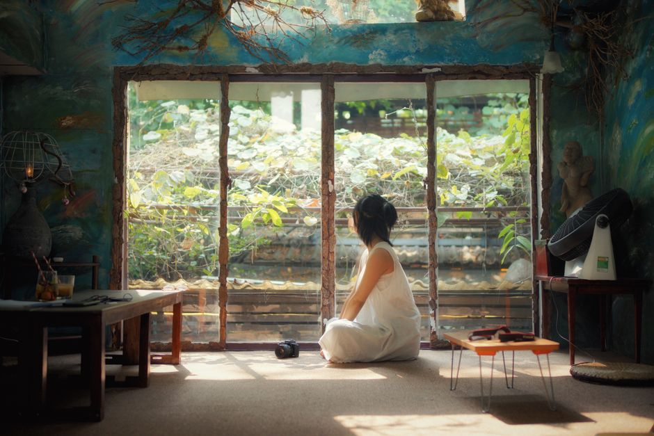 A serene scene featuring a woman in a white dress, sitting cross-legged by a window, with a calm, natural backdrop.