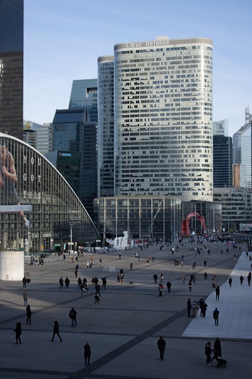 A large plaza with people walking around and buildings in the background