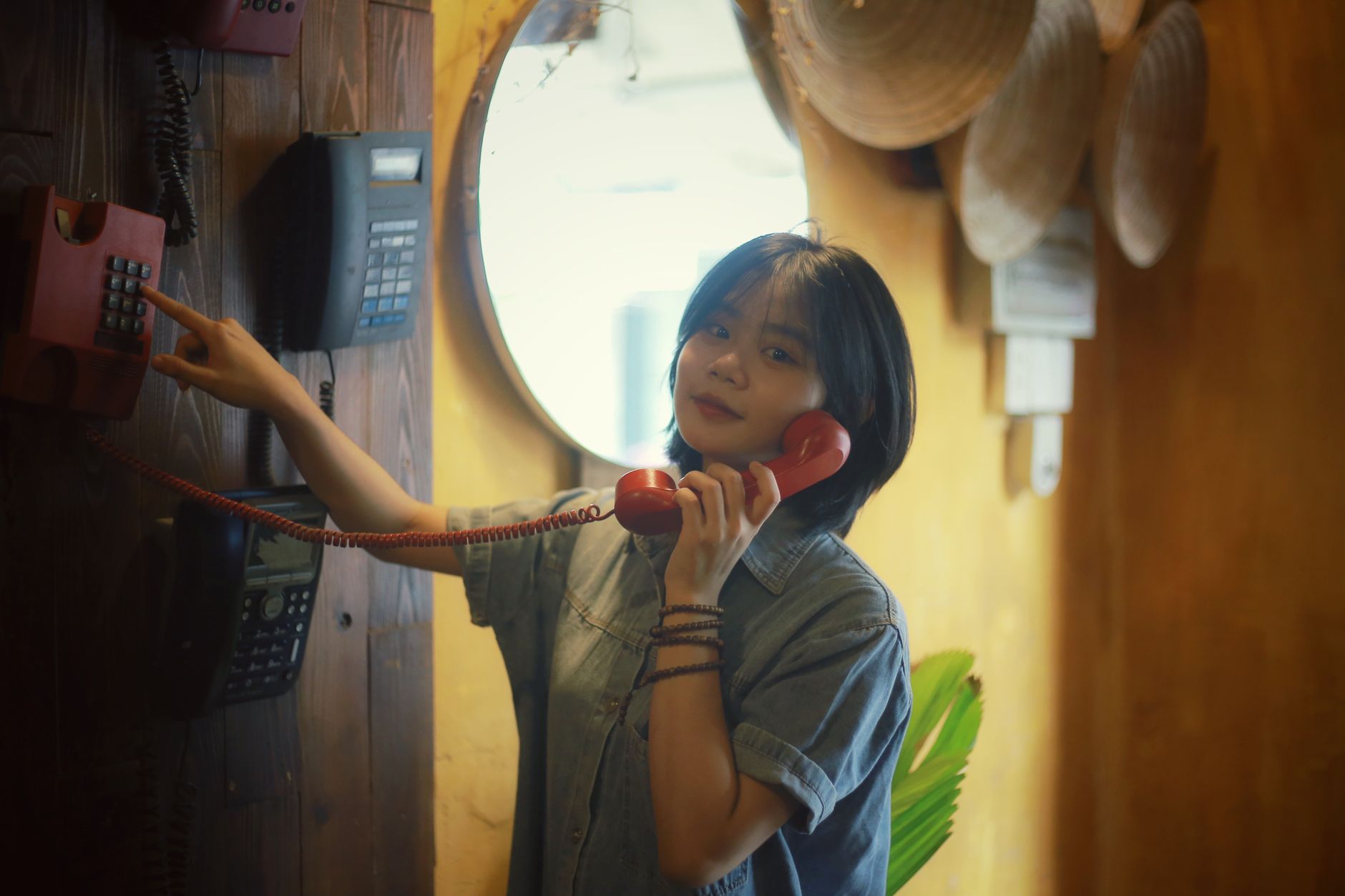 A young woman in a jean shirt using vintage telephones in a stylish indoor setting.