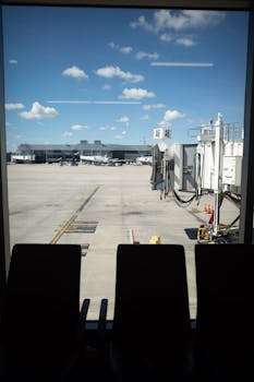 View of an airport tarmac through a window with empty chairs in the foreground.