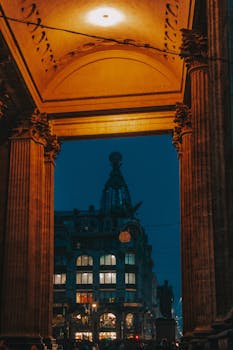 Majestic columns framing a view of St. Petersburg's historic buildings illuminated in the night.