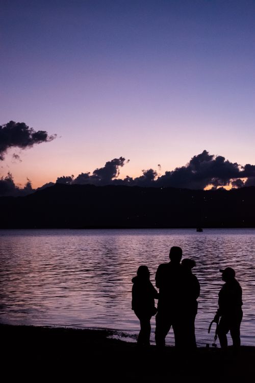 Free A group silhouetted against a dusk sky by a serene lakeshore. Stock Photo