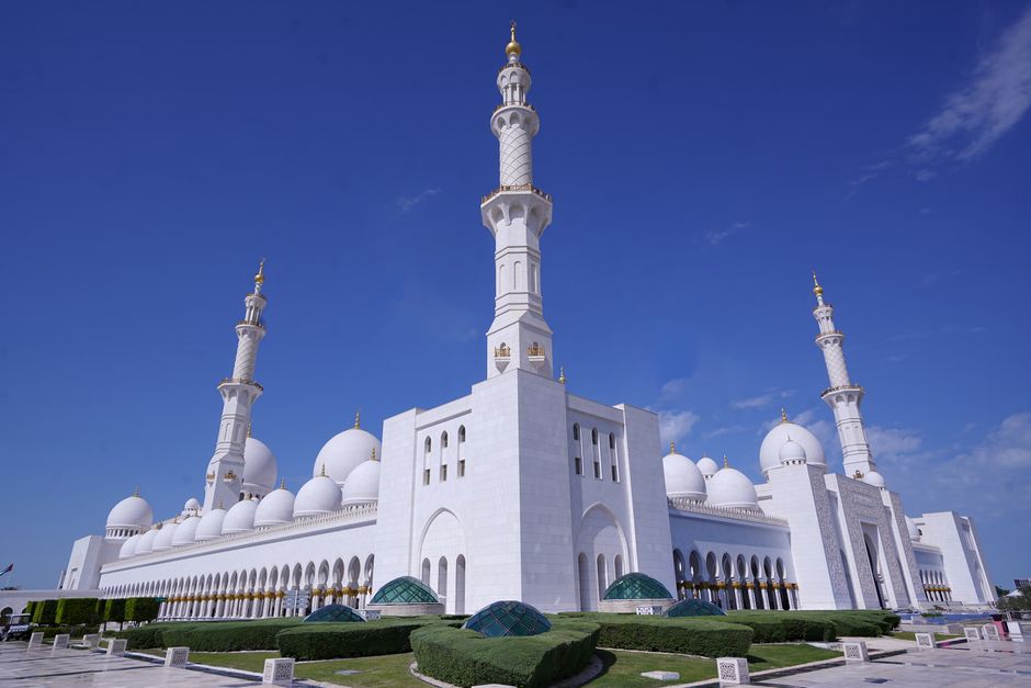 Stunning view of the Sheikh Zayed Grand Mosque showcasing its iconic white domes and minarets against a clear blue sky.