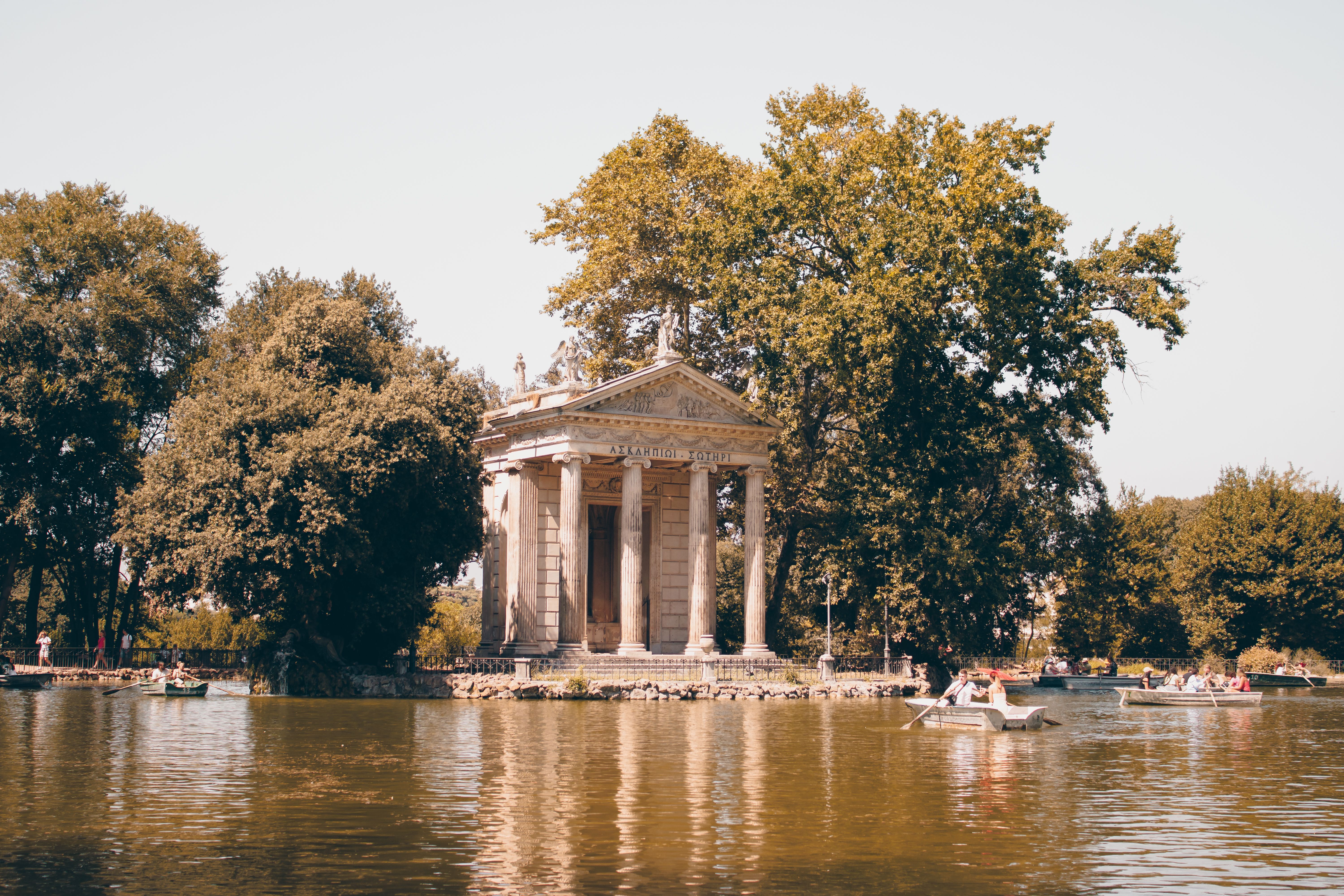 Scenic view of the Temple of Aesculapius surrounded by lush trees and a tranquil lake in Villa Borghese, Rome.