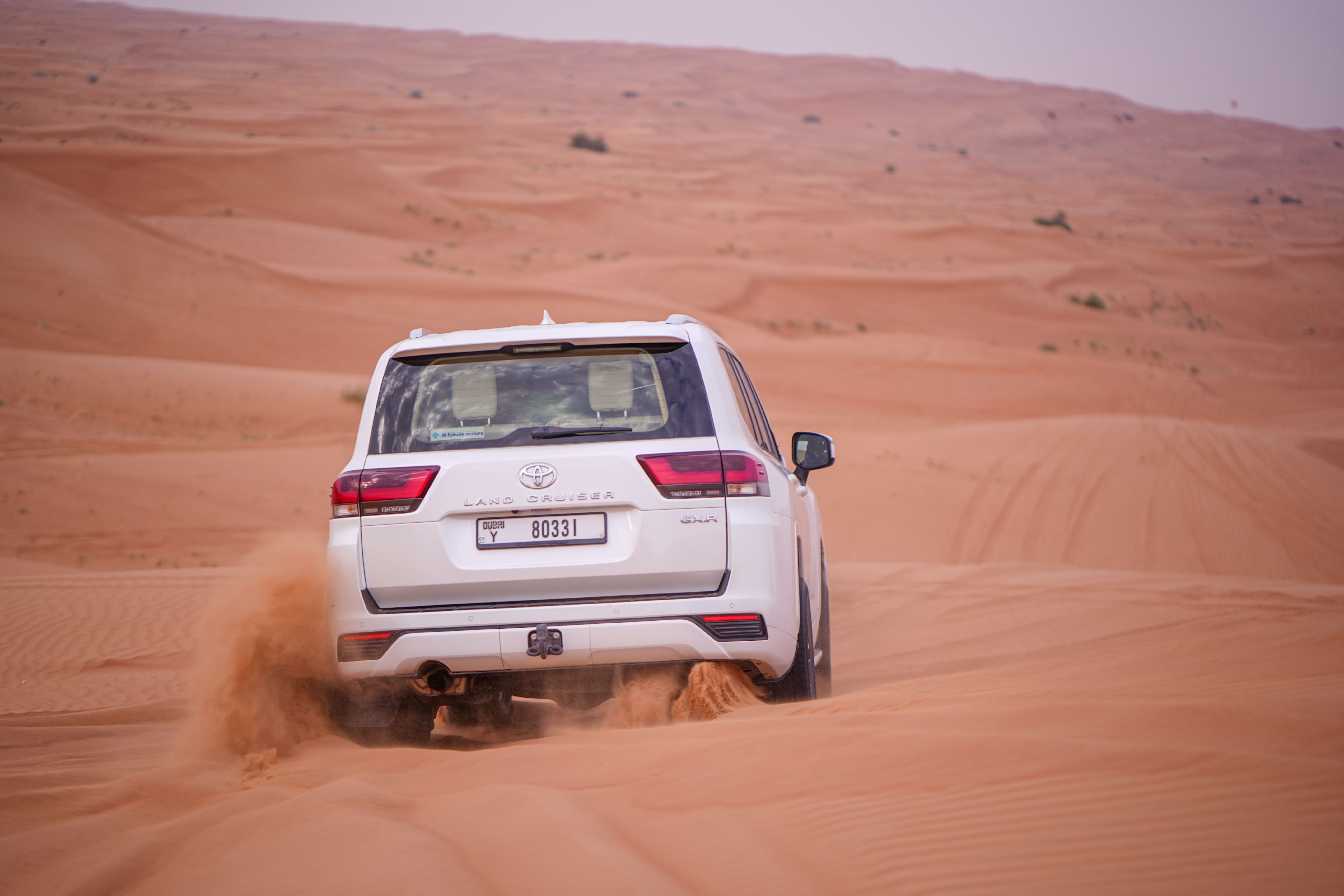 A Toyota Land Cruiser drives actively through a vast desert, showcasing offroad capabilities.
