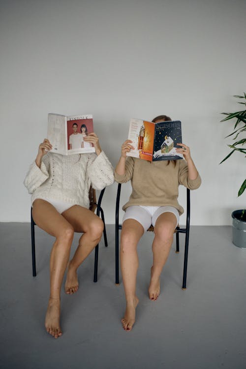 Two women sitting on chairs reading magazines