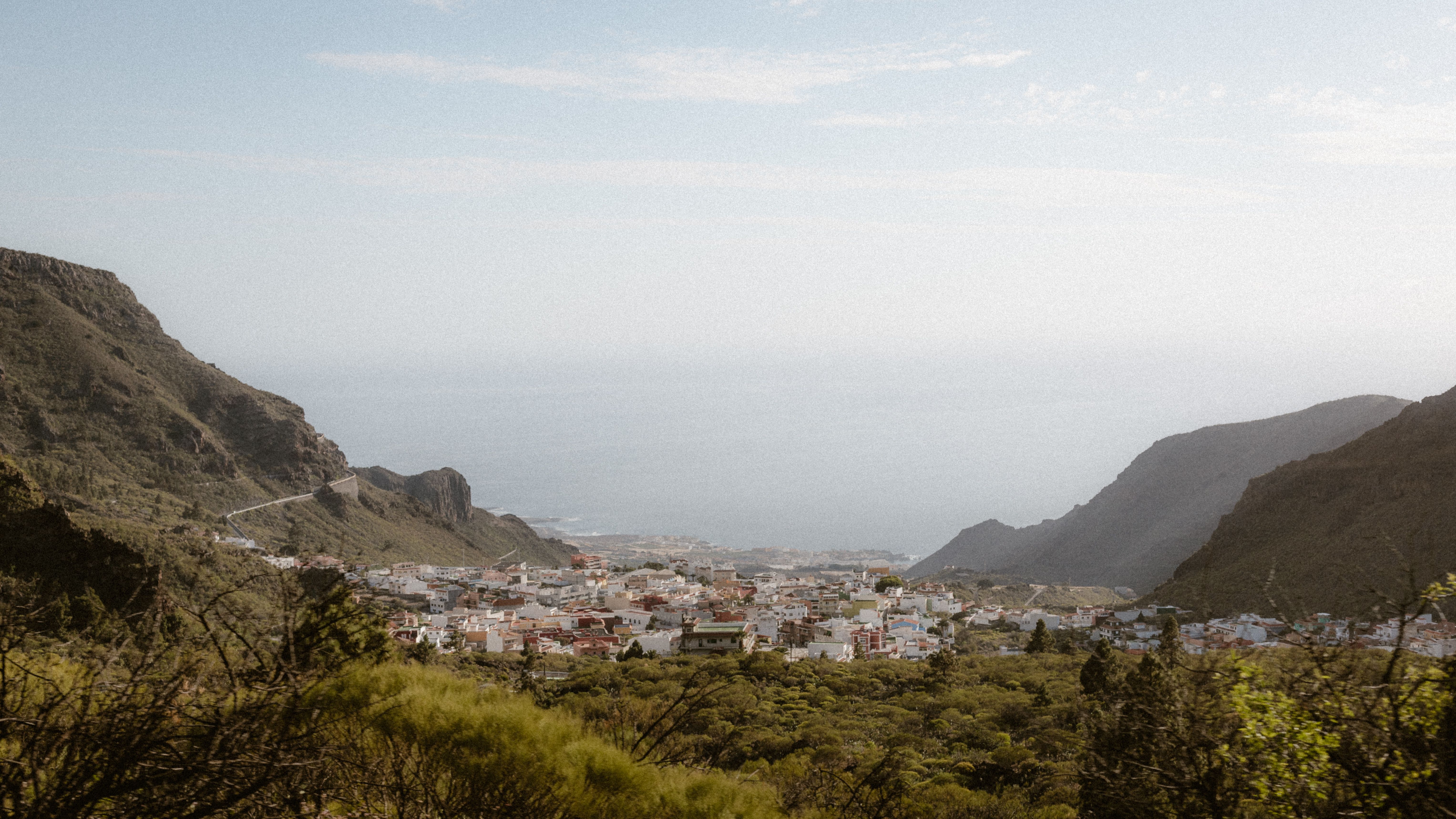 A picturesque mountain valley town with lush greenery and distant sea view in Tenerife, Spain.