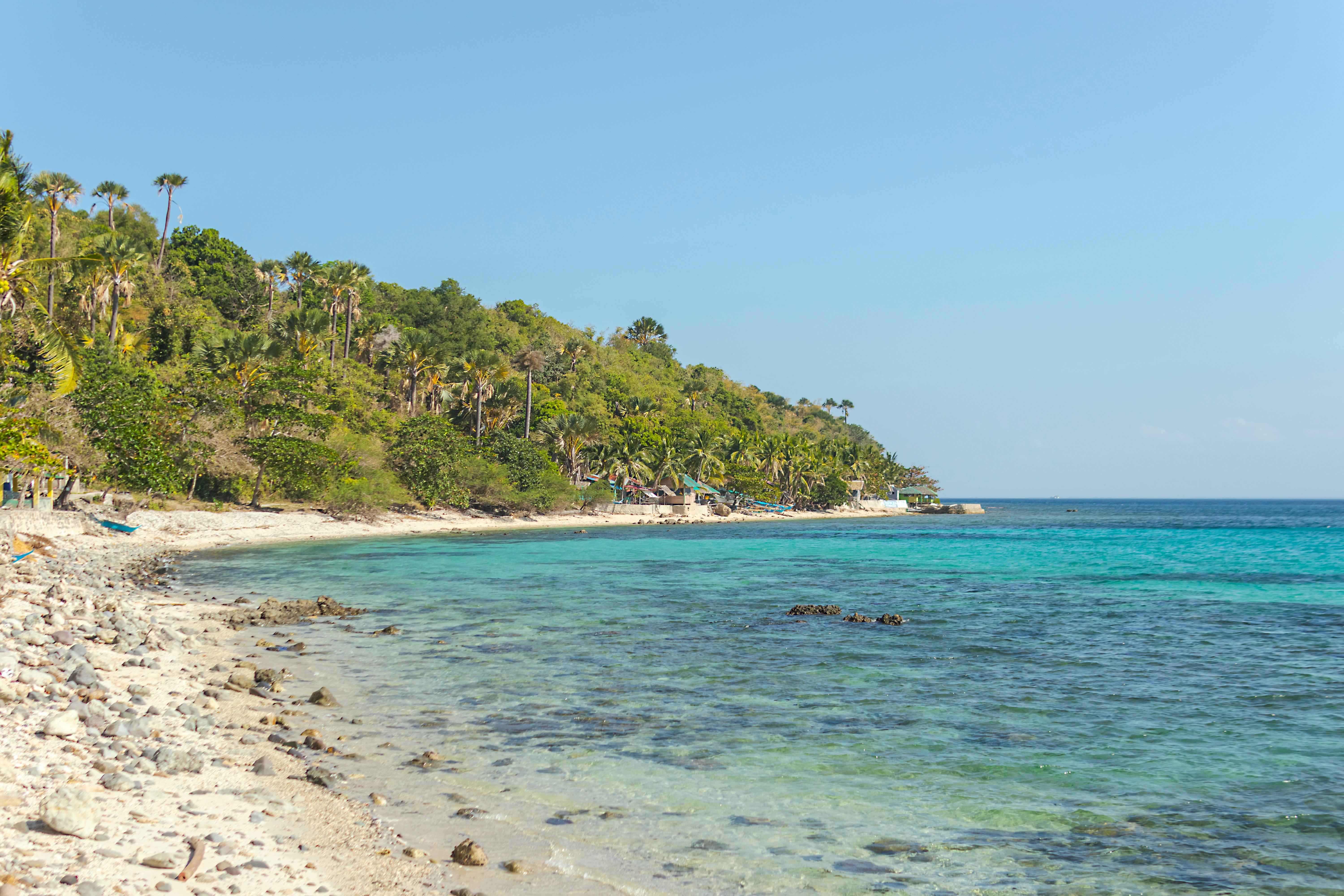 Idyllic tropical beach with lush green hills and crystal-clear ocean waters under a bright blue sky.