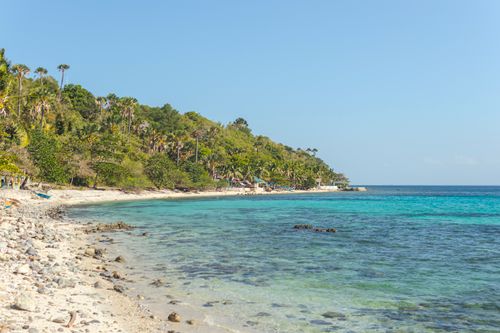 Free Idyllic tropical beach with lush green hills and crystal-clear ocean waters under a bright blue sky. Stock Photo