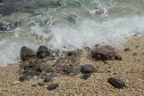 Free Close-up of waves hitting rocky beach with pebbles on a sunny day. Stock Photo