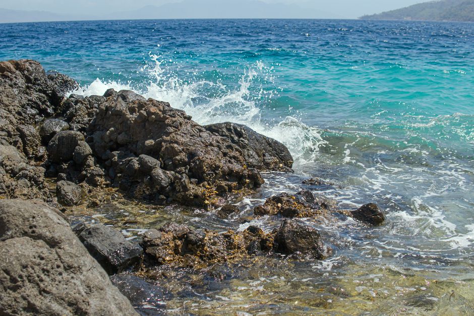 Dynamic coastal scene with waves crashing onto rocky shore, showcasing vibrant summer seascape.