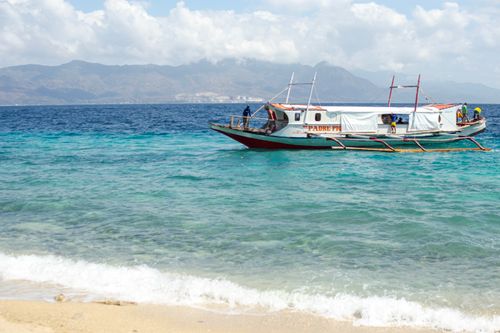 Free Vibrant coastal scene featuring a traditional boat anchored near a sandy beach under sunny skies. Stock Photo