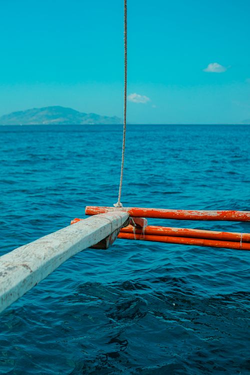 Free A serene view of a traditional boat outrigger over the blue sea with distant islands in the background. Stock Photo