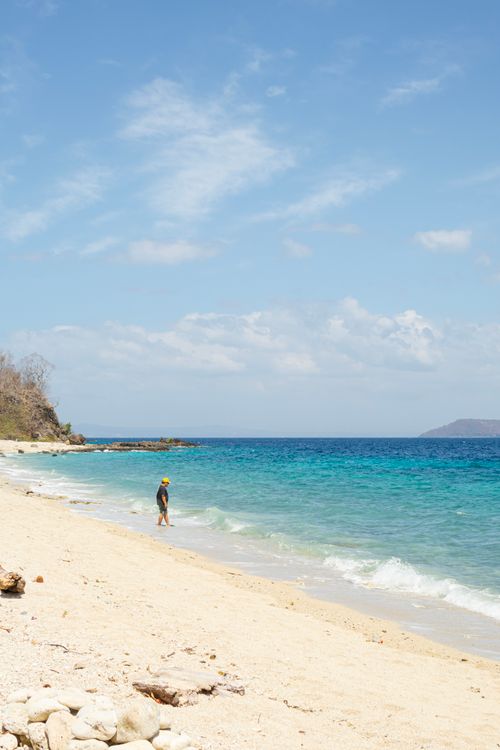 Free A lone person walking on a tranquil sandy beach with blue sea on a sunny day. Stock Photo