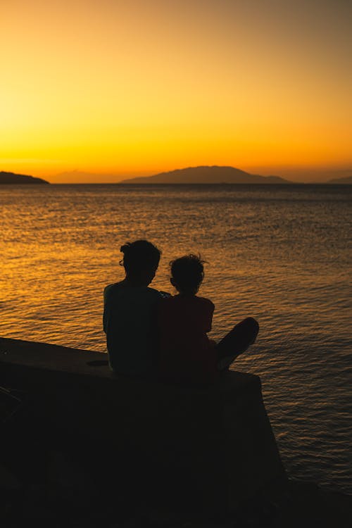 Two people sitting on a wall looking at the sunset