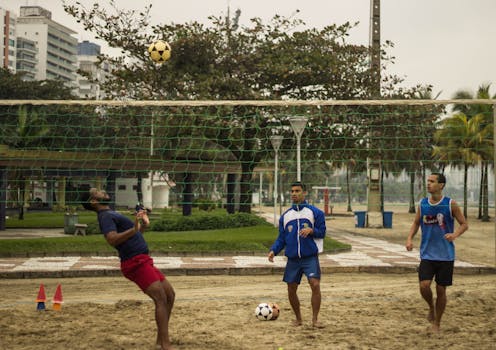 Three men engaging in a casual soccer game in an urban park environment, featuring net and ball.