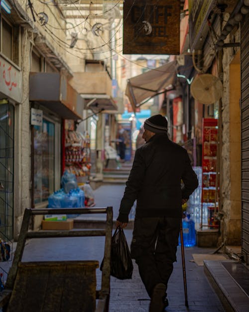 A man walking down a narrow alleyway with a cane