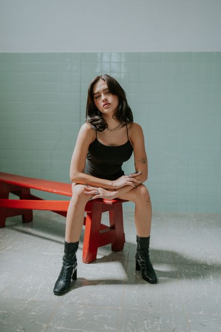 A fashionable woman in black attire sitting on a red bench indoors, expressing modern style.