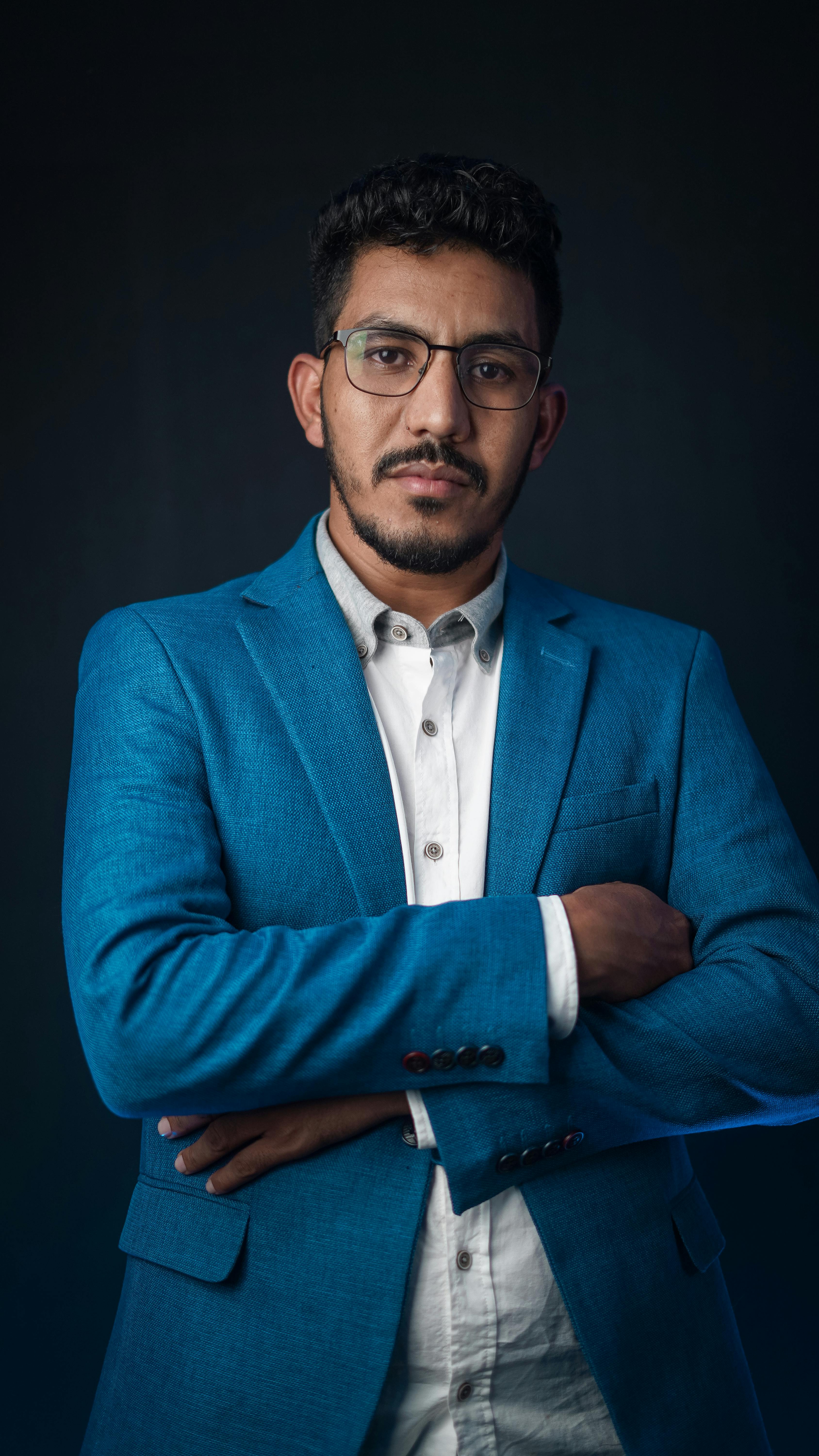 Elegant portrait of a serious businessman with glasses in a blue suit against a dark background.