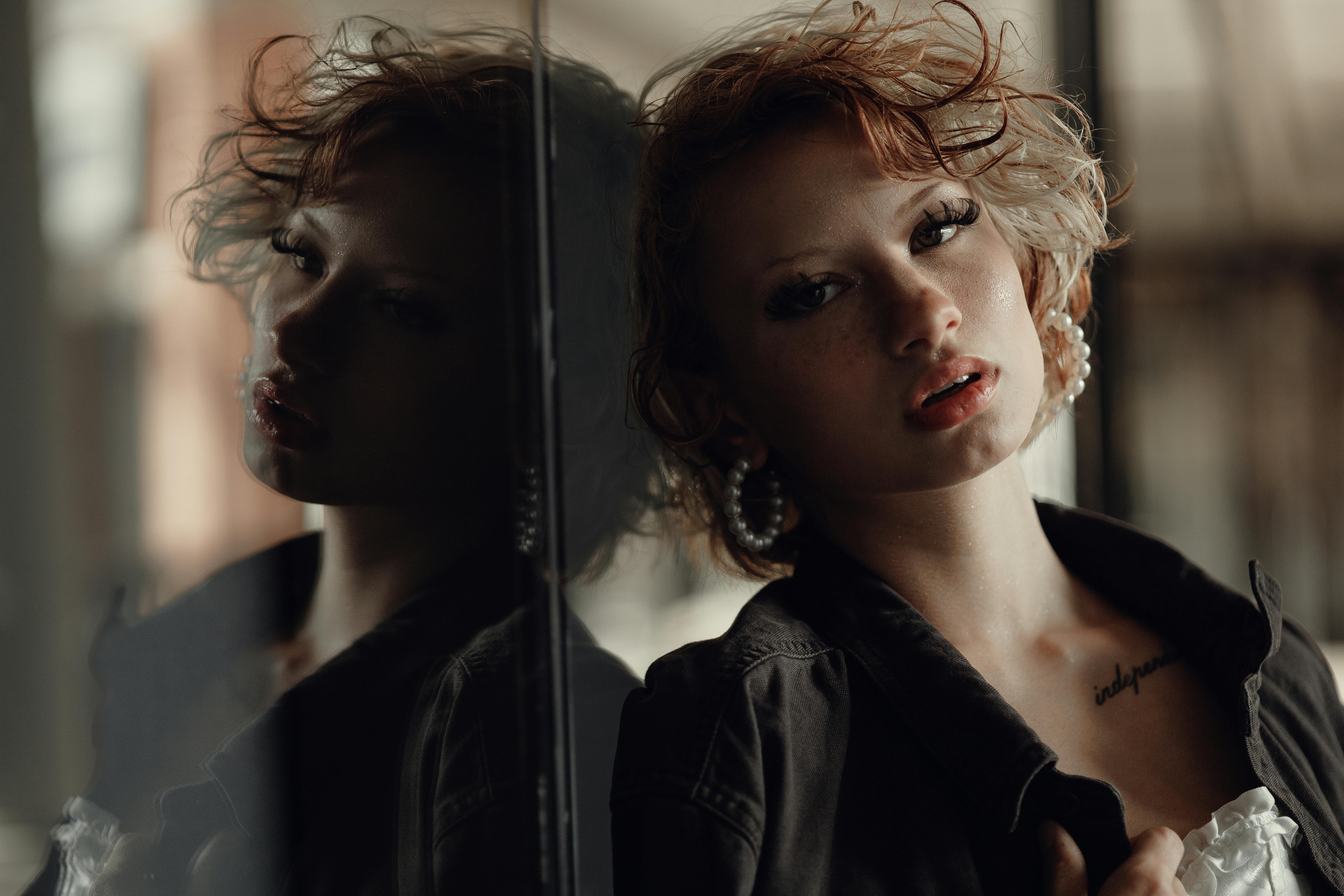 Striking portrait of a woman with short hair and earrings, reflecting on glass.