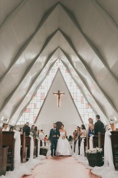 Beautiful indoor wedding ceremony in a church with a bride and groom walking down the aisle surrounded by guests.