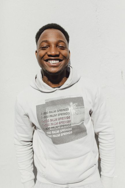 Cheerful young man in a hoodie posing outdoors against a bright wall.