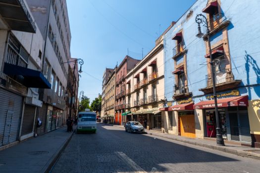 Vibrant urban street scene in Mexico City with colorful buildings and parked vehicles under clear skies.
