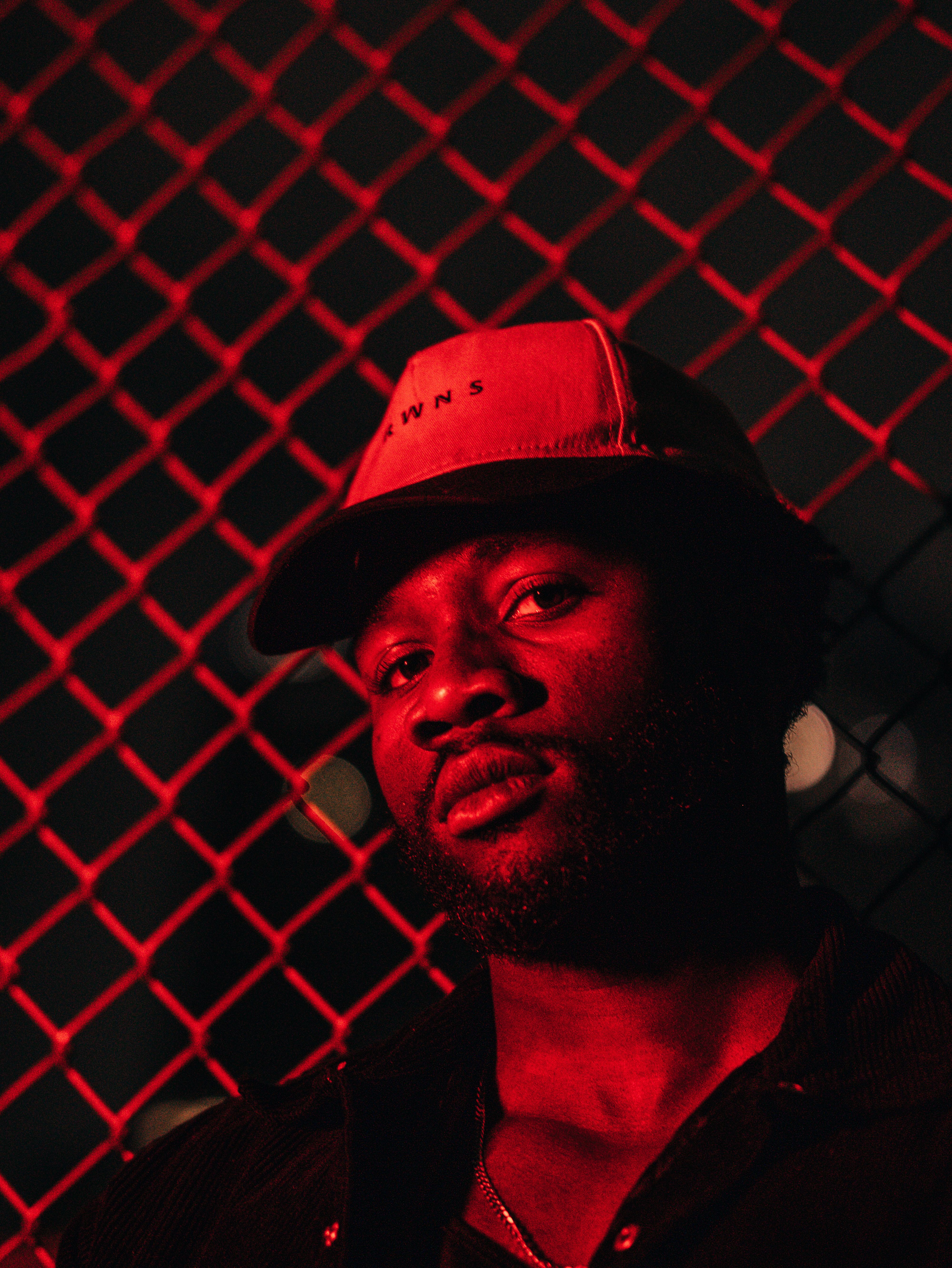 A stylish portrait of a man at night with red lighting and a chain link fence.