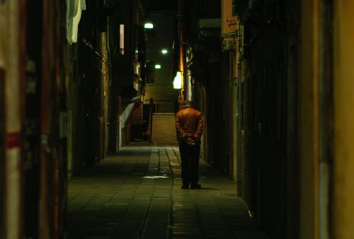 Free A senior man walks alone in a narrow alleyway in Venice, Italy, at night. Stock Photo