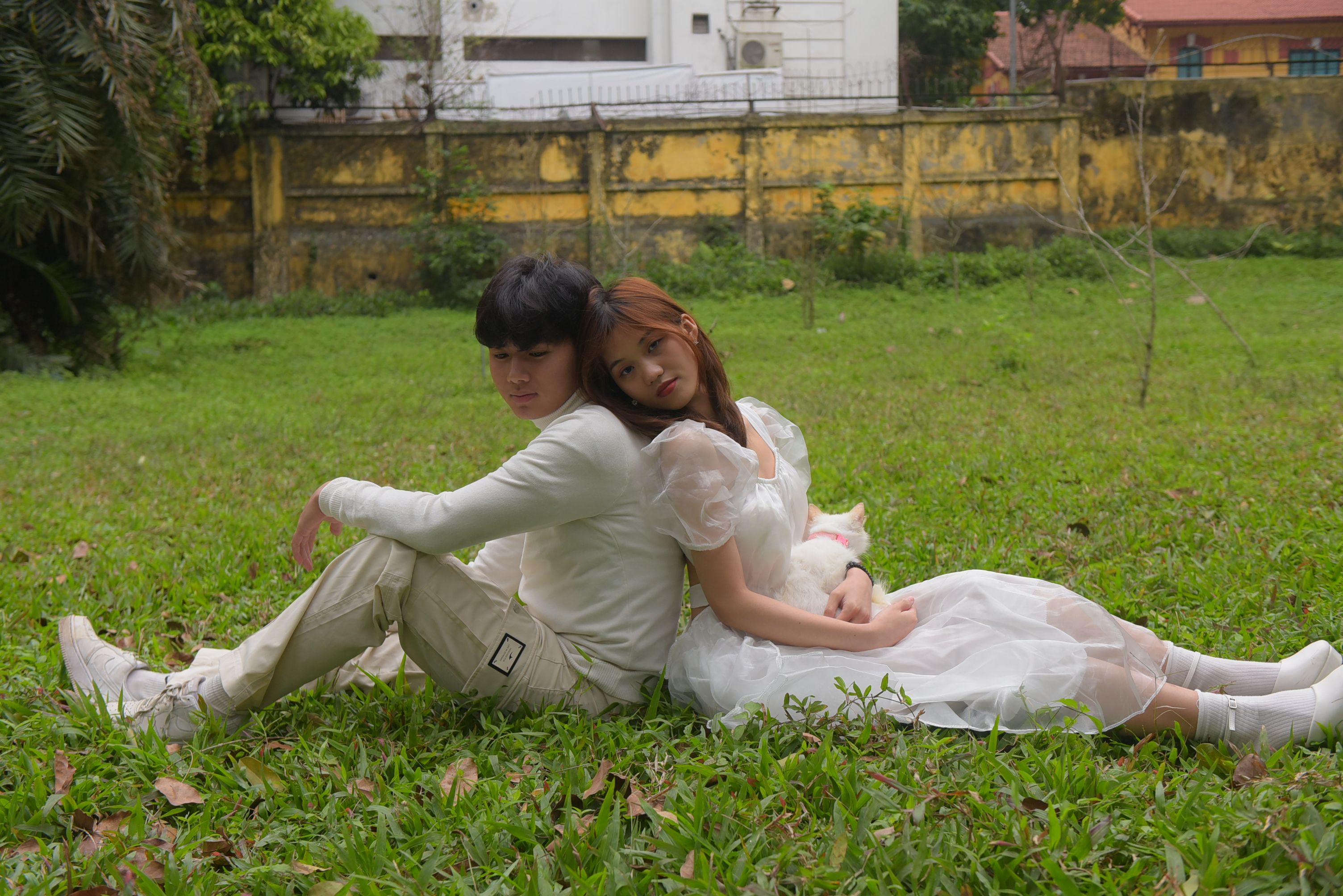 Asian couple sitting back-to-back on a grassy lawn, exudes love and relaxation.