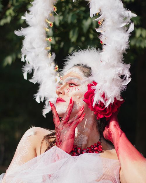 Free Captivating portrait of a woman with theatrical makeup and feathered headpiece, posing outdoors. Stock Photo
