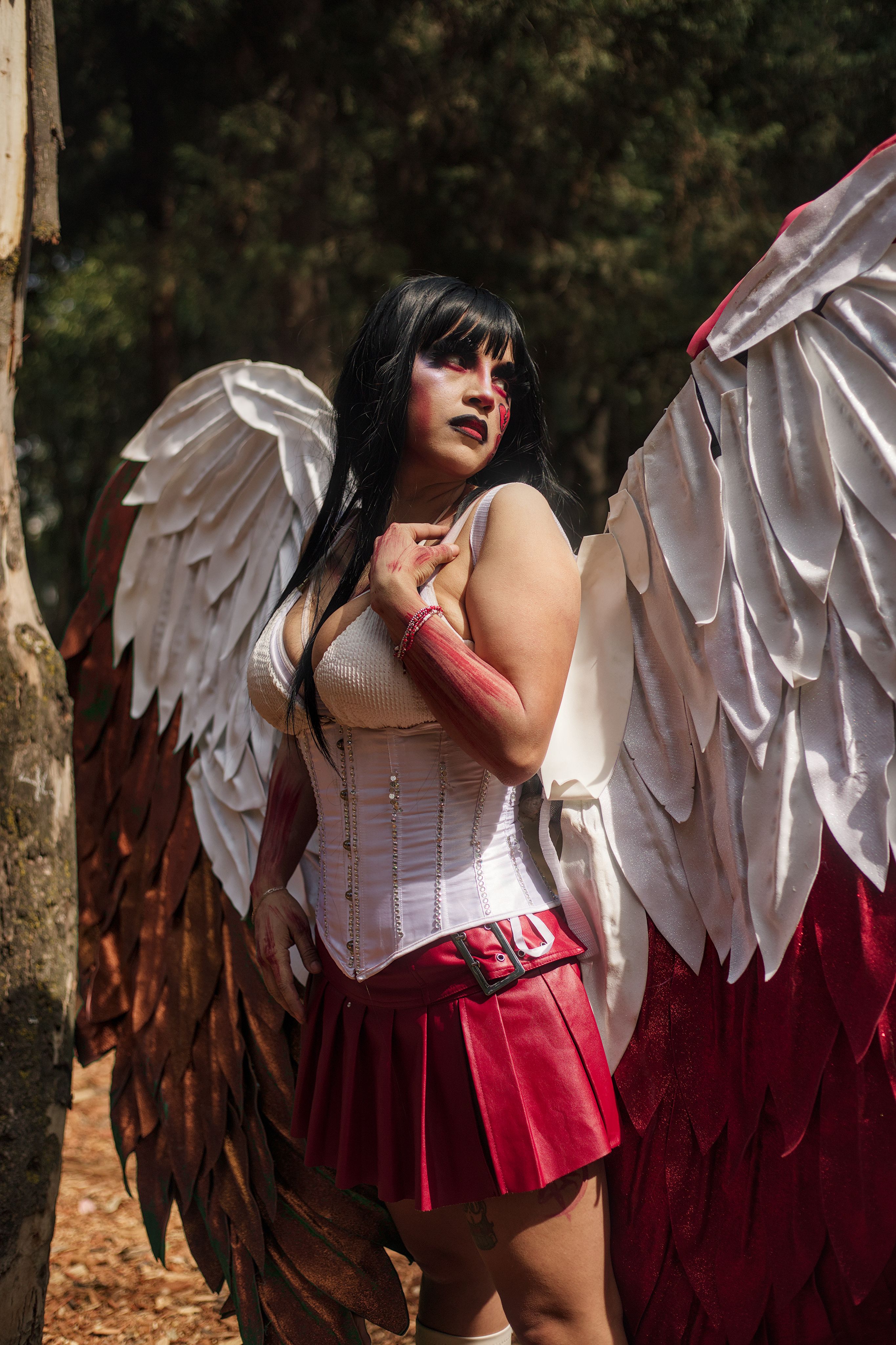 A woman in angelic cosplay with wings, posing in a forest in daylight.