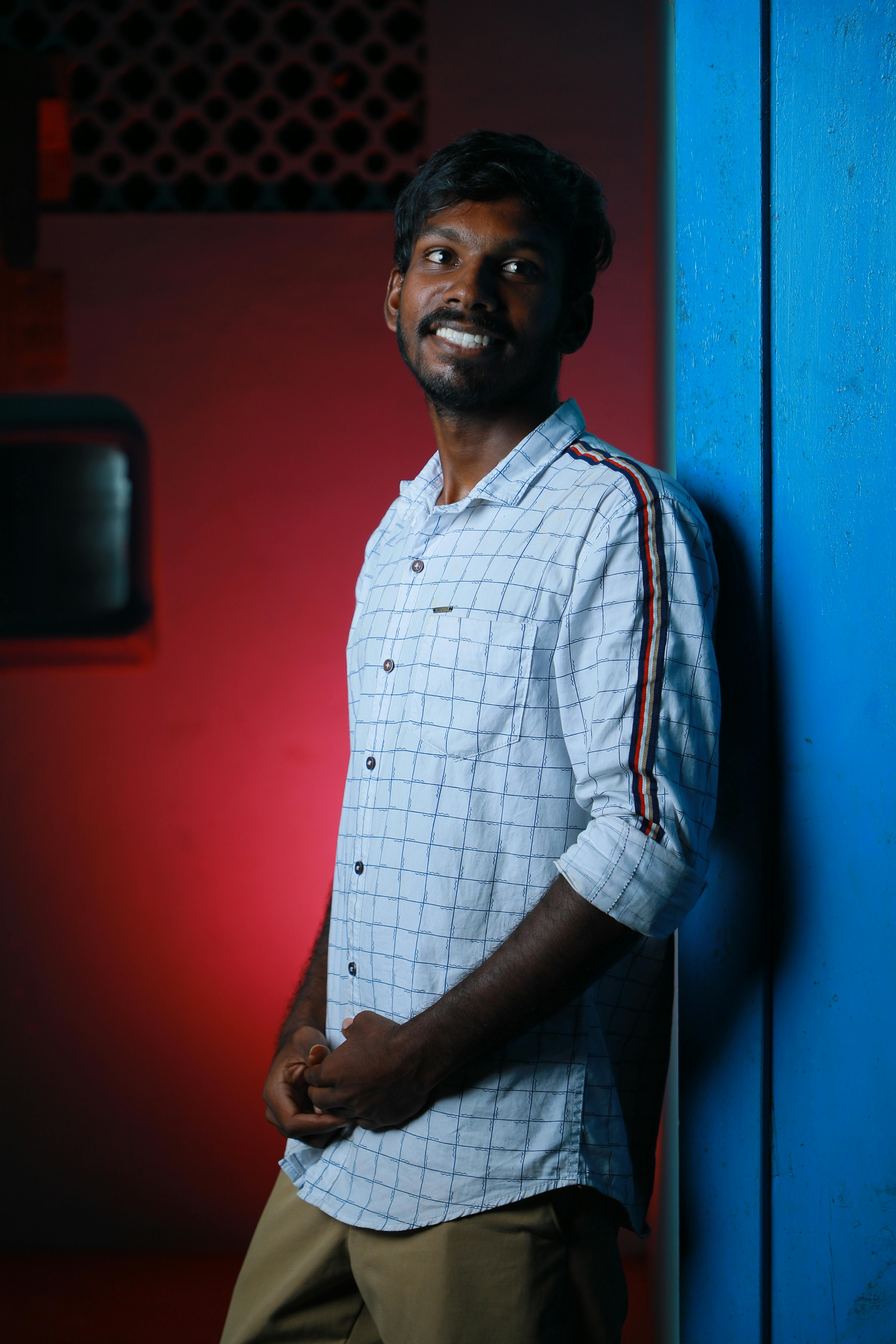 Captivating portrait of a man with mustache smiling and leaning against a blue wall indoors.