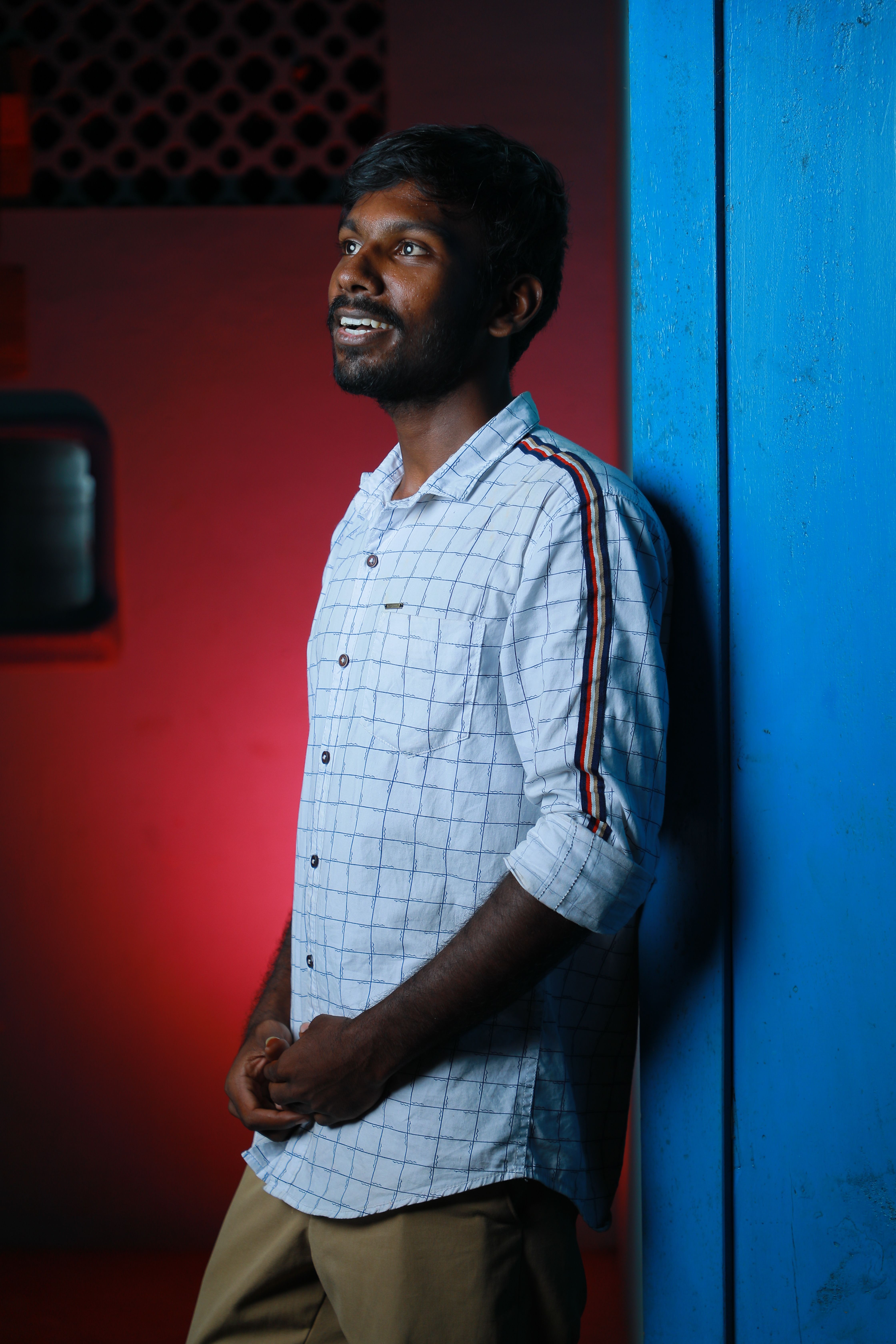 Portrait of a man with a beard and mustache, smiling while leaning against a blue wall at night.