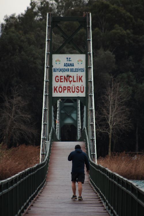 Free A man walks across Gençlik Köprüsü footbridge in Adana, Türkiye, amidst a natural setting. Stock Photo