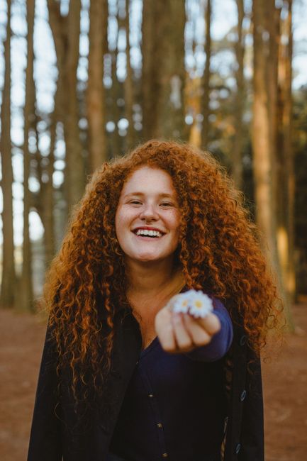 Portrait of a happy woman with curly hair holding daisies in a serene forest.