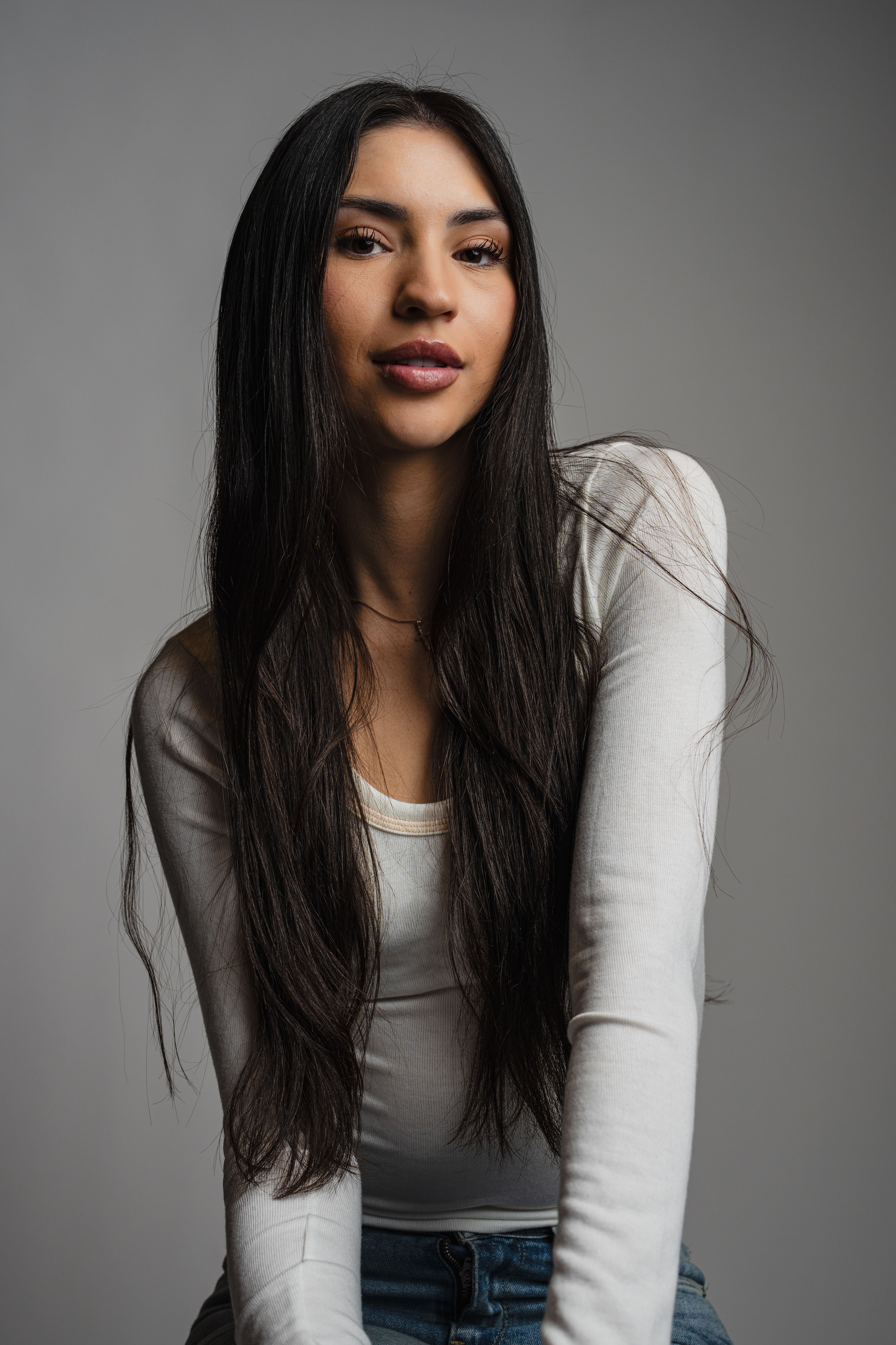 Portrait photo of a woman with long hair wearing a white top and jeans in a studio setting.