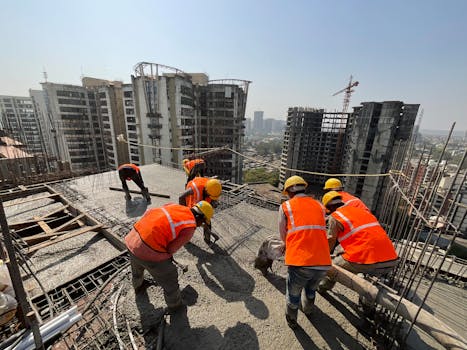 Workers in safety gear building a skyscraper with a city skyline backdrop.