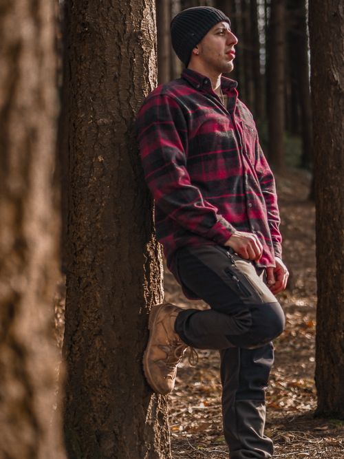 Free Adult man leaning on tree in forest wearing a hat and plaid jacket. Stock Photo