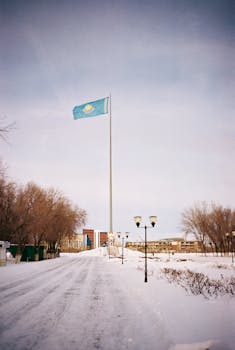 Tall Kazakhstan flagpole on a snowy street in Aktobe, Kazakhstan, during winter.