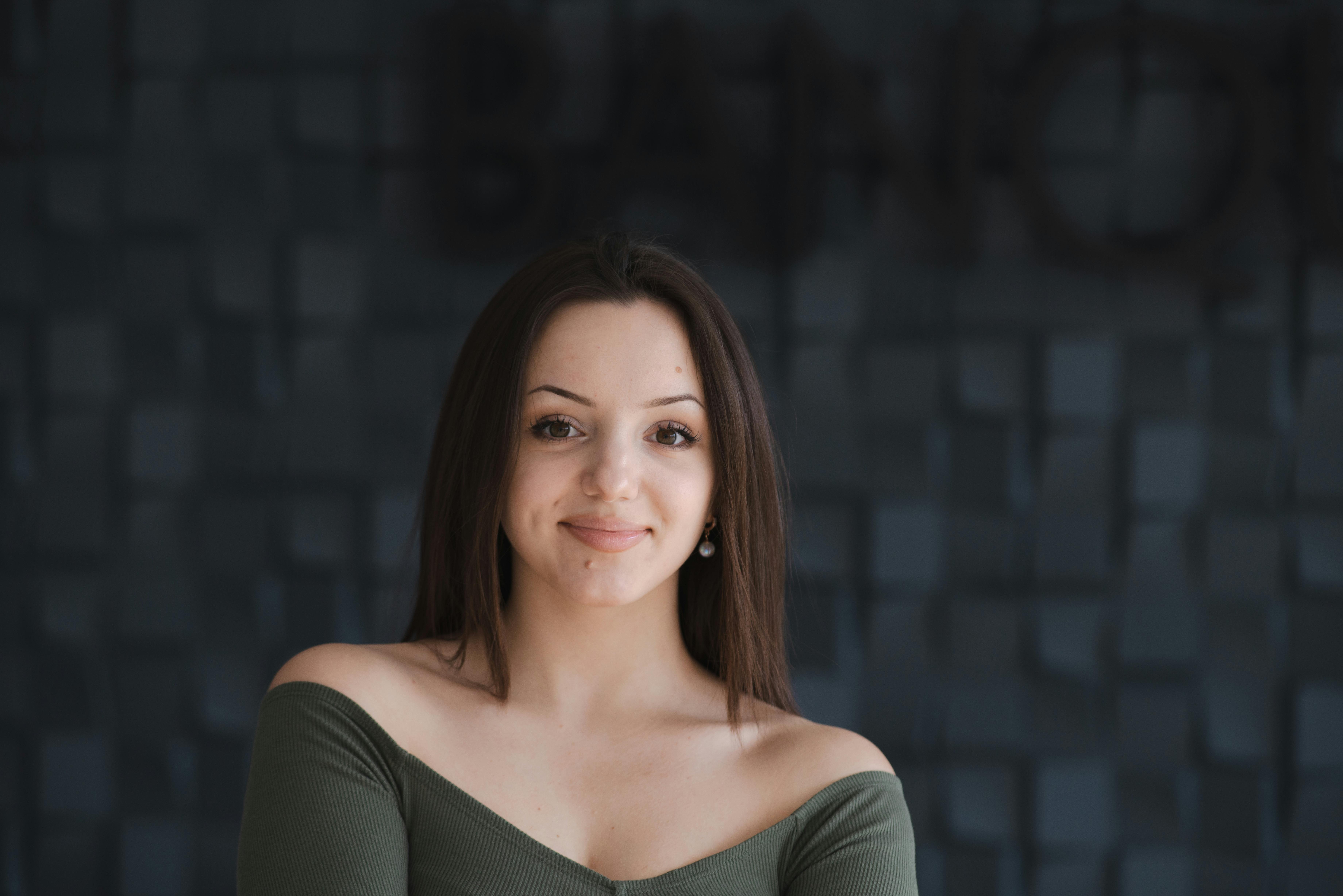 A young woman smiles confidently in a stylish portrait with a dark textured background.