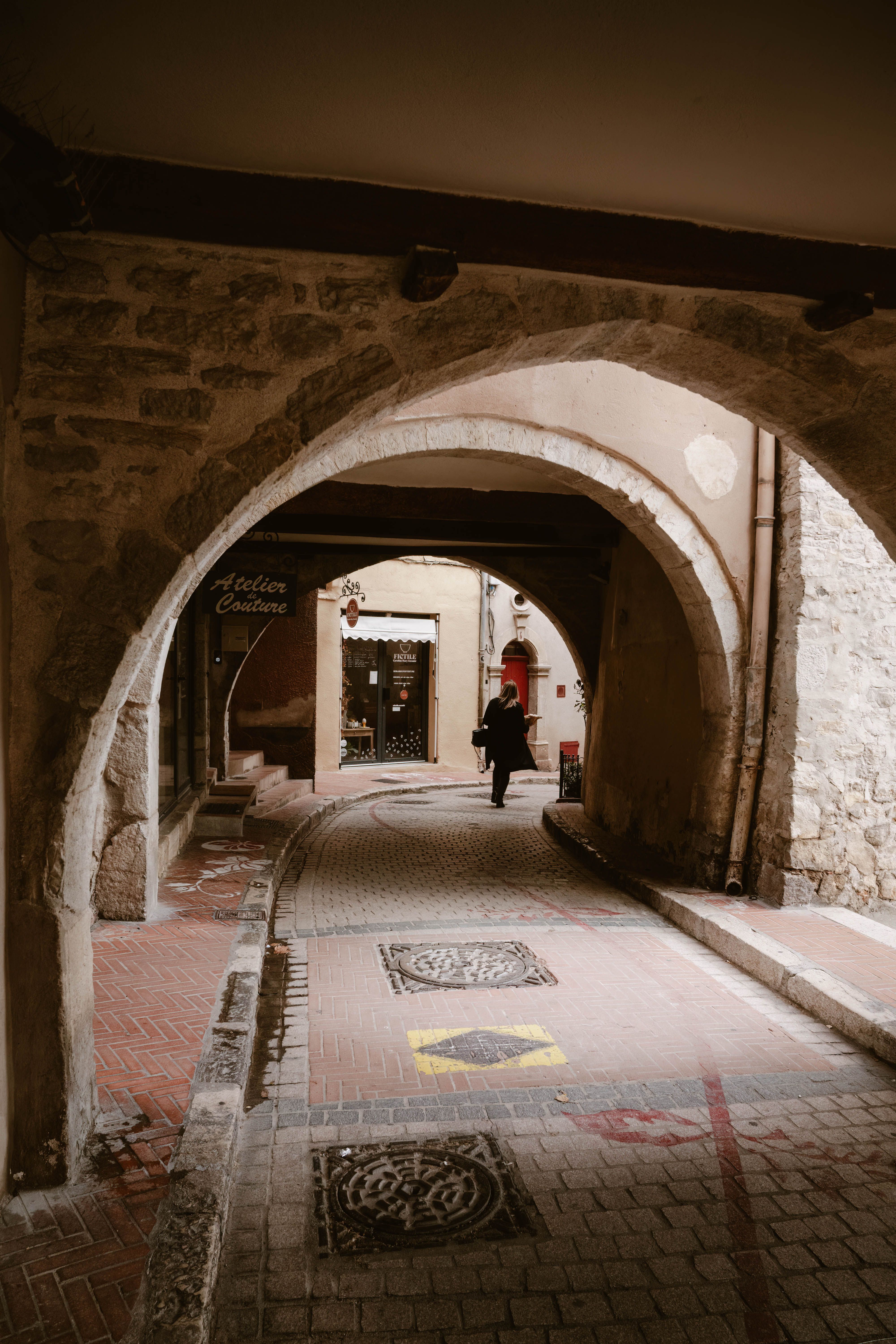 Cobblestone path under stone arches in Le Revest-les-Eaux, Provence, France. Person walking in historic ambiance.