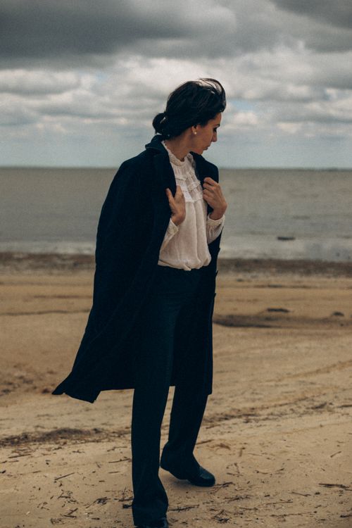 Free A stylish woman in a black coat poses on a serene beach. Fashion photography emphasizing elegance. Stock Photo