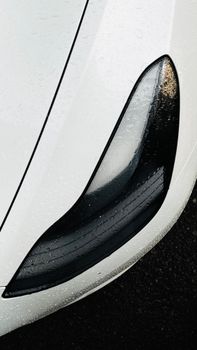 Detailed view of a white car headlight with raindrops, showcasing modern design.