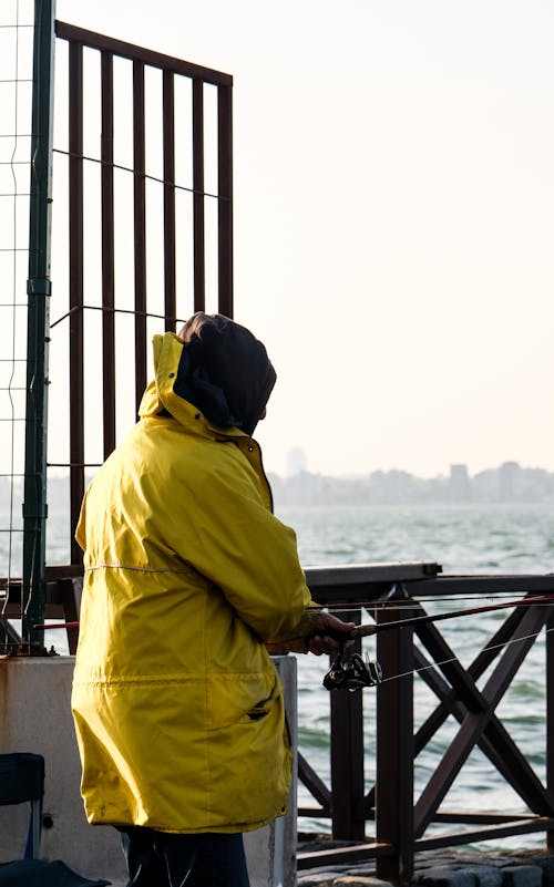 A man in a yellow jacket is standing on a pier