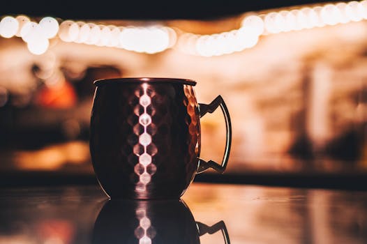 一个铜杯放在反光表面上，背景是温暖的散景灯光