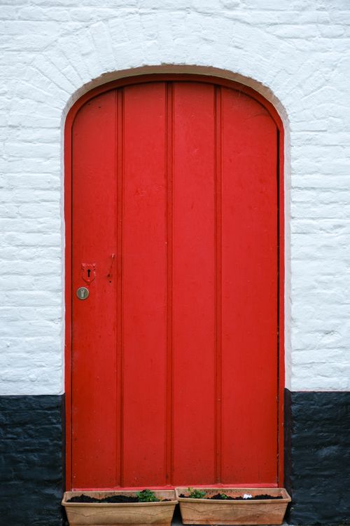 Free Striking red arched door set in a white brick wall with black trim, offering a pop of color. Stock Photo