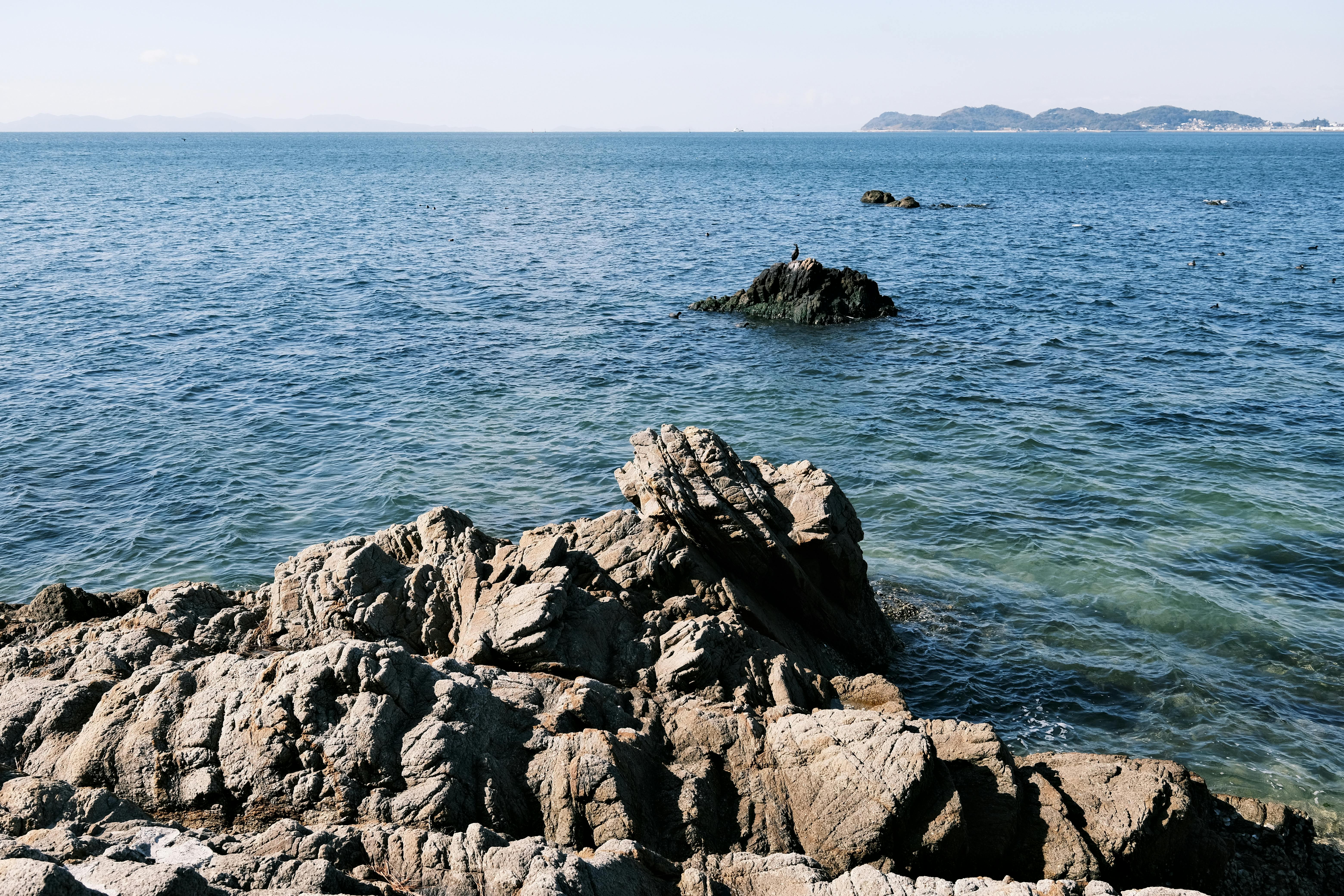 Stunning rocky seashore in Gamagori, Japan with clear blue ocean and distant islands.