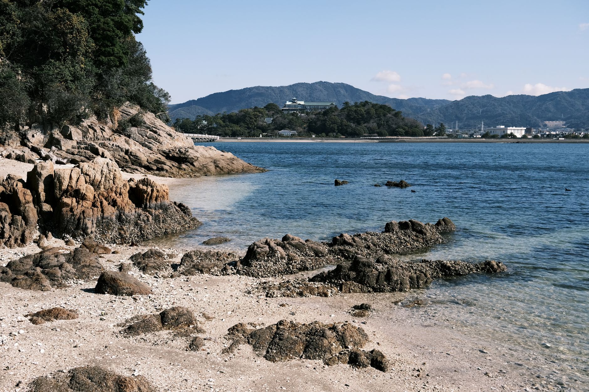 Explore the stunning rocky seashore of Gamagori, Aichi, Japan with clear blue waters and distant mountains.