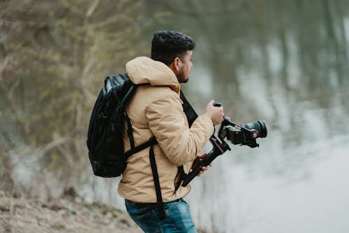 A man with a backpack and camera is standing by the water